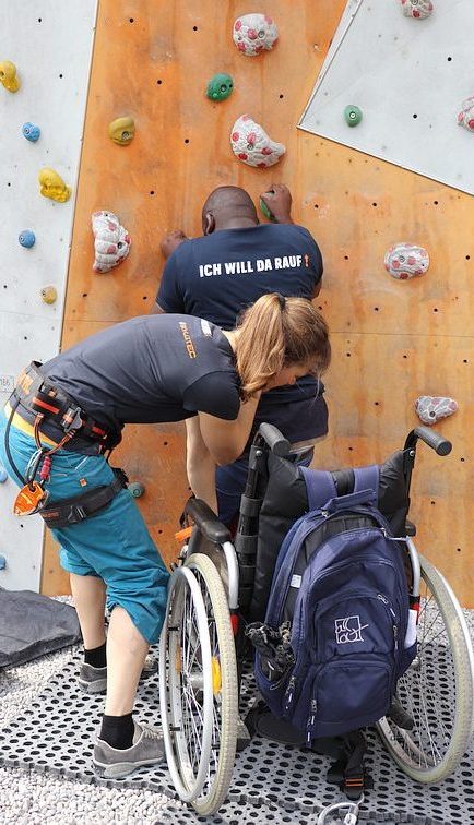 Mann mit Handicap bewegt sich aus dem Rollstuhl an eine Kletterwand