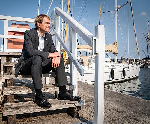 Ministerpräsident Daniel Günther sitzt auf einer Holztreppe am Hafen