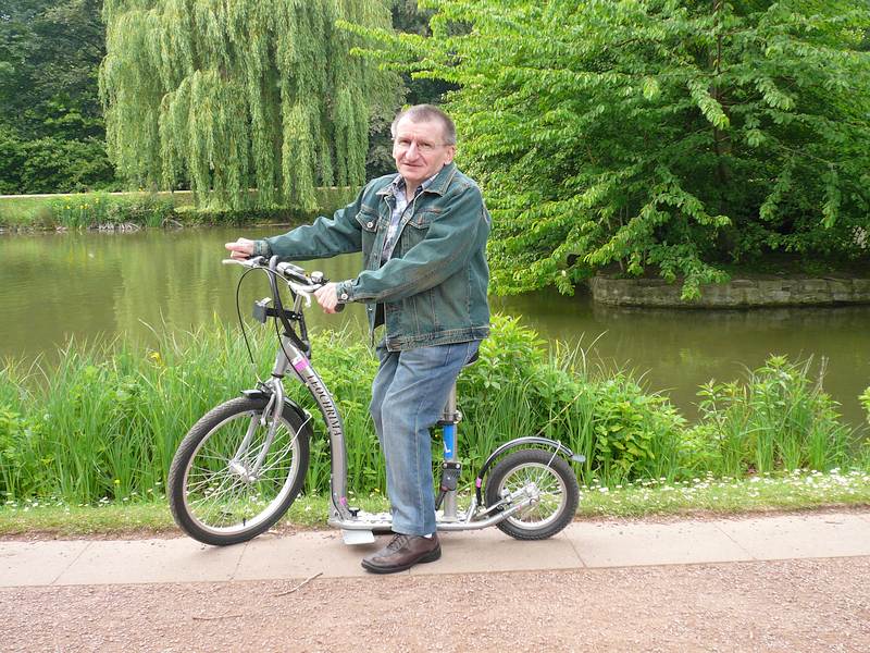 Ein kleinwüchsiger Mann auf einem angepassten Fahrrad vor einem Teich