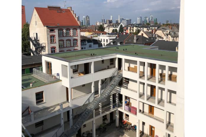 Moderner weiß gestrichener Wohnblock mit mehreren Wohneinheiten, über Eck gebaut, mit Innenhof.