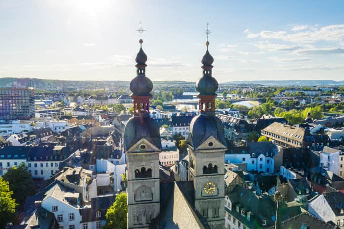 Stadtansicht von Koblenz von oben fotografiert. Im Vordergrund befinden sich 2 Kirchtürme, im Hintergrund erkennt man den Rhein.