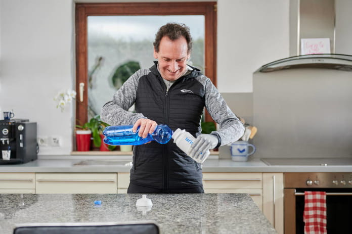 Ein Mann gießt aus einer Plastikflasche Wasser in eine Trinkflasche, die er schräg mit seiner Prothesenhand hält.