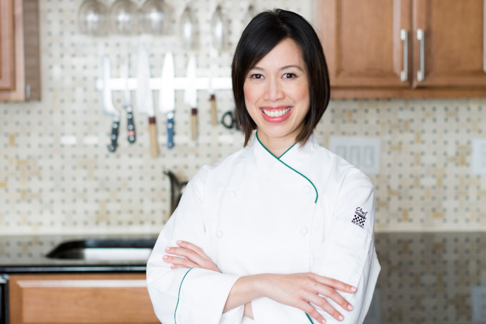 Portrait von Christine Ha in einer weißen Kochjacke, im Hintergrund eine Küche