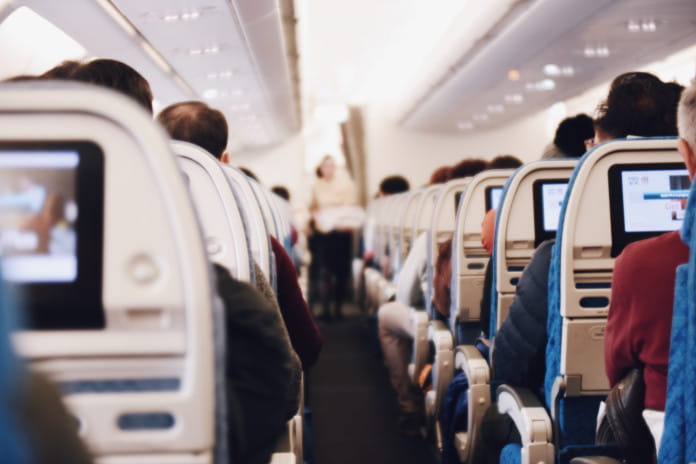 Blick von hinten nach vorn in der Flugzeugkabine. Alle Passagiere sitzen auf ihren Plätzen, vor ihnen sind Bildschirme angebracht. 