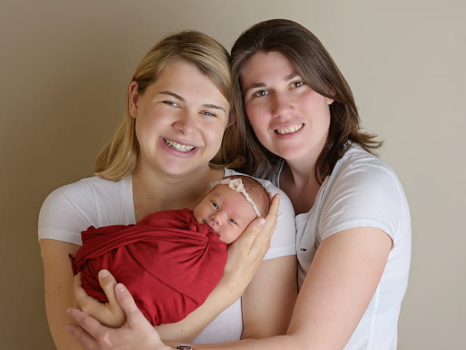 Bianca Brosch, ihre Frau und die Tochter stehen eng bei einander und lächeln in die Kamera. 