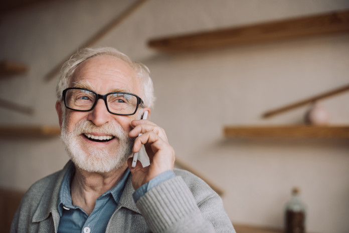 Ein älterer Mann hält ein Telefon ans Ohr und lacht.