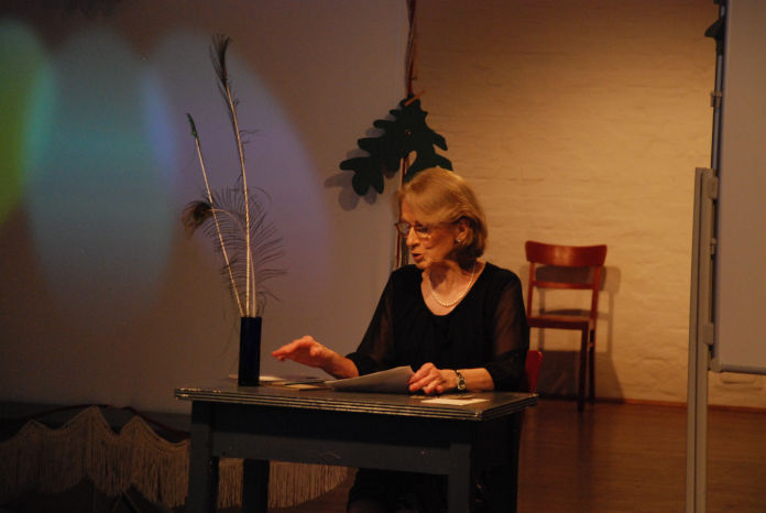 Eine ältere Dame sitzt an einem Tisch und liest vor.