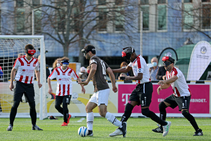Eine Szene aus dem Blindenfußball, wo Männer mit speziellen Brillen um den Fußball kämpfen. 