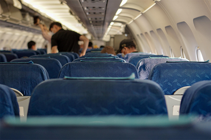 Blick aus einer Sitzreihe im Flugzeug nach vorn, die Bezüge der Sitze sind blau. Menschen im Hintergrund. 