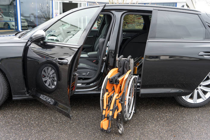 Fahrzeug in der Seitenansicht, ein zusammengefalteter Rollstuhl steht vor einer Schiebetür im hinteren Bereich, bereit zum Verladen