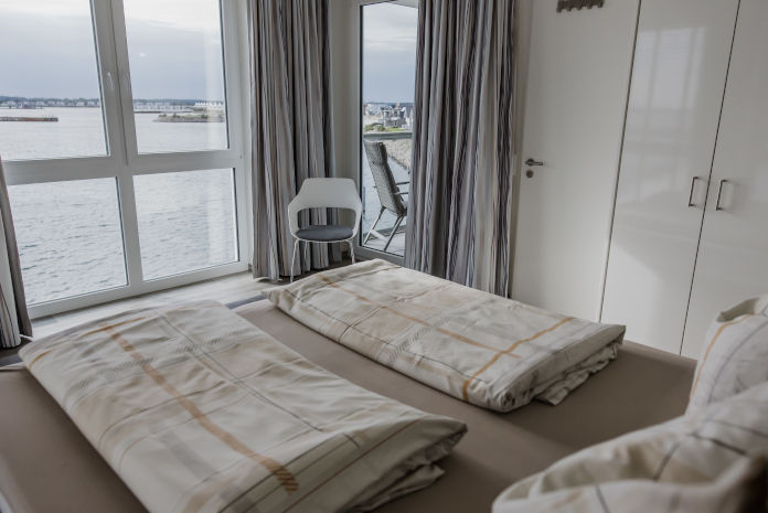 Schlafzimmer eines Appartements, aus dessen Fenster die Ostsee zu sehen ist.