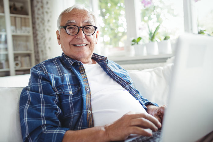 Ein älterer Herr sitzt auf der Couch mit einem Laptop auf dem Schoß