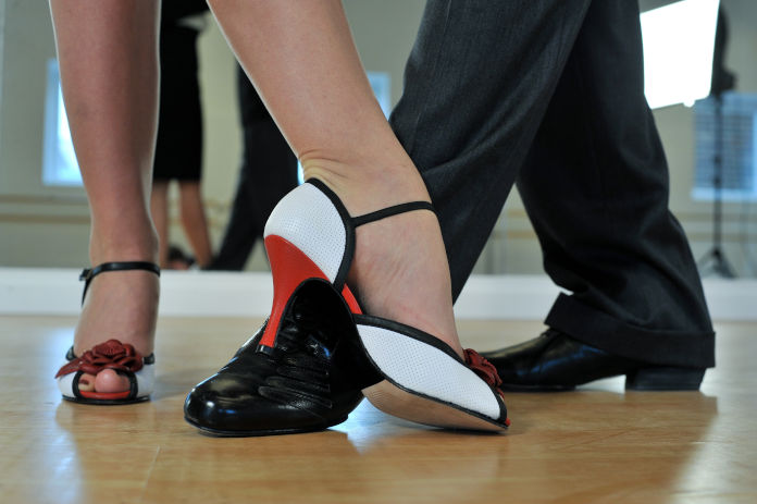 Das Foto zeigt die Fußstellung eines Tanzpaares. Der rechte Fuß der Frau steht gerade. Der linke Fuß steht leicht gebeugt vor dem linken Fuß des Mannes. Der rechte Fuß des Mannes steht gerade zum Standfuß der Frau.