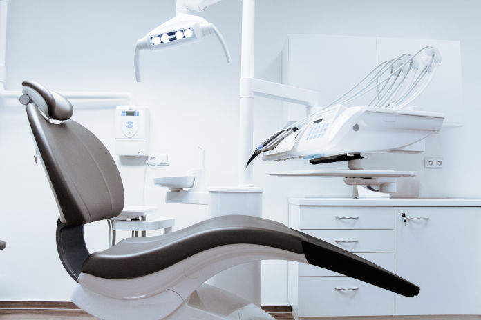 Ein Zahnarztstuhl in einer Zahnarztpraxis, man sieht diverse Gerätschaften.