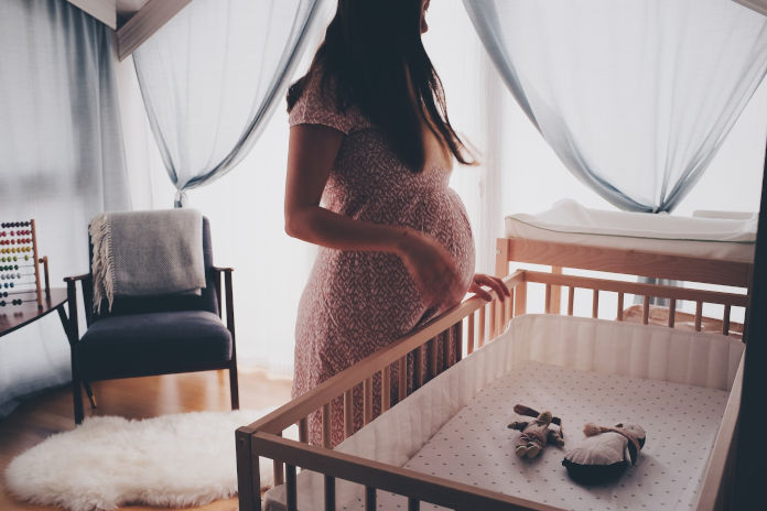 Eine schwangere Frau steht vor einem Kinderbett .