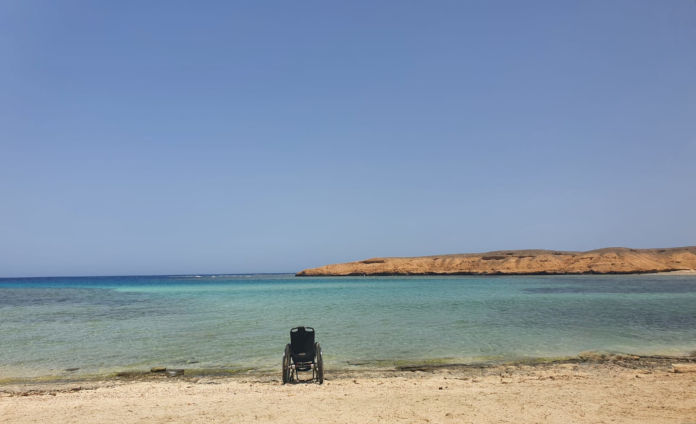 Ein Rollstuhl mit breiten Reifen steht am Ufer. 