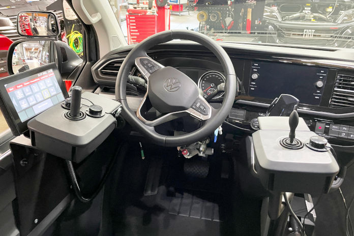 Ein Cockpit von einem VW T6. Links und rechts neben dem Lenkrad sind Konsolen mit Joysticks zu sehen sowie eine Steuereinheit. 