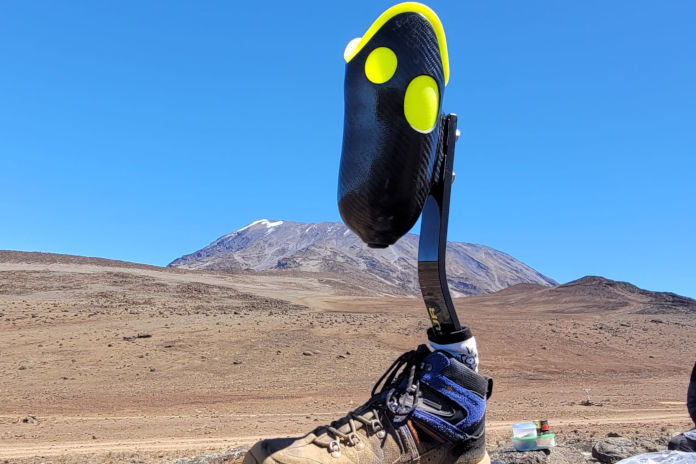 Das Foto zeigt eine Unterschenkelprothese inklusive Schuh stehend auf einem Stein. Im Hintergrund ist der Kilimandscharo.