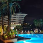 Ein Hotel in Form eines Flugzeuges Concorde. Im Vordergrund ein beleuchteter Pool umgeben von Palmen. Das Foto wurde bei Dunkelheit aufgenommen.