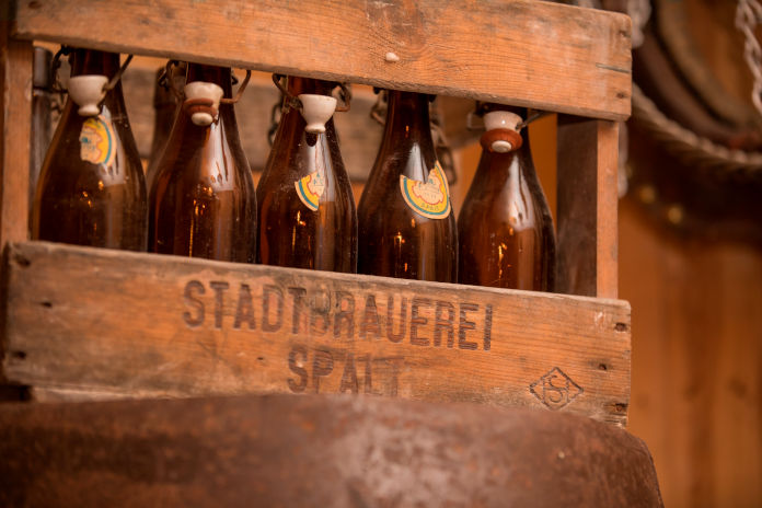 Fünf braune Bierflaschen nebeneinanderstehend in einer Holzkiste mit der Aufschrift Stadtbrauerei Spalt.