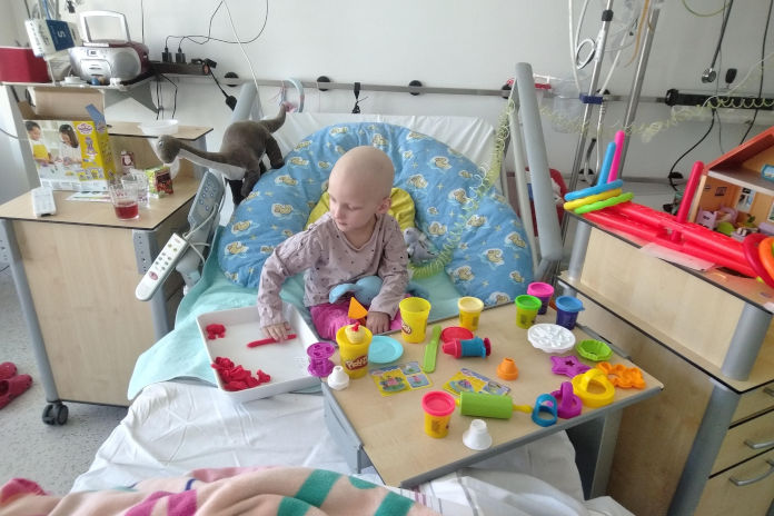Ein kleines Mädchen sitzt in einem Krankenhausbett , welches mit Spielsachen gefüllt ist.
