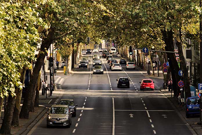 Eine vier-spurige Straße, auf der Autos fahren. Links und rechts stehen Bäume. 