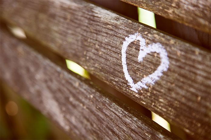 Eine Lehne einer Holzbank, darauf ist ein Herz mit Kreide gemalt. 