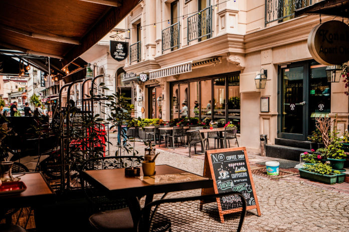 Ein Tisch vor einem Café in einer Straße mit Altbauten. Auf der Straße steht ein Aufsteller des Cafés.