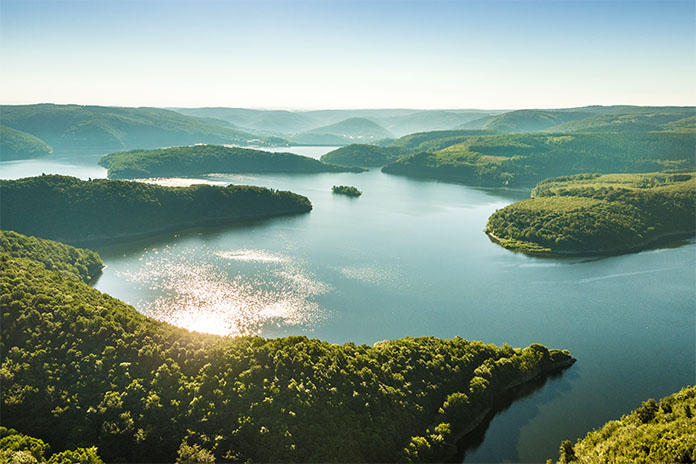 Der Nationalpark der Eifel von oben aufgenommen. Erkenntlich ist das Mittelgebirge mit Bäumen und Wasser im Sonnenlicht aufgenommen.