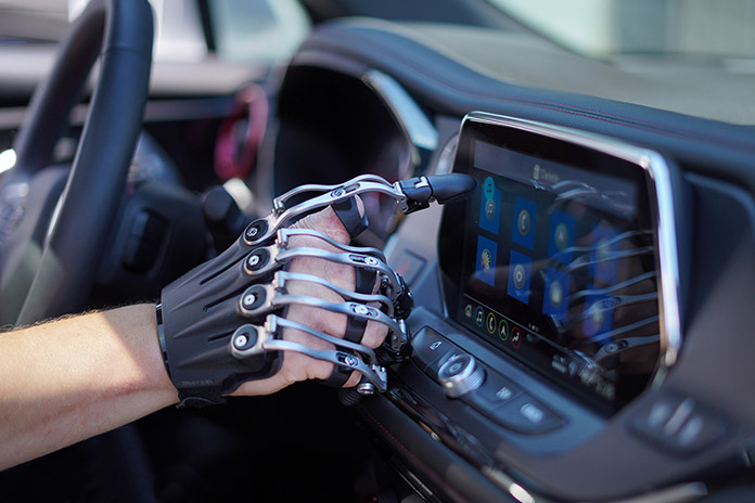 Eine Fingerprothese an einer rechten Hand mit vier Fingern. Mit dem Zeigefinger wird an einen Touchscreen im Auto getippt. 