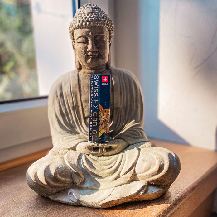 Eine sitzende Steinfigur. Ein Buddha. In den Händen des Buddhas steht eine aufrechte Verpackung mit der Aufschrift SWISS FX CBD ÖL.