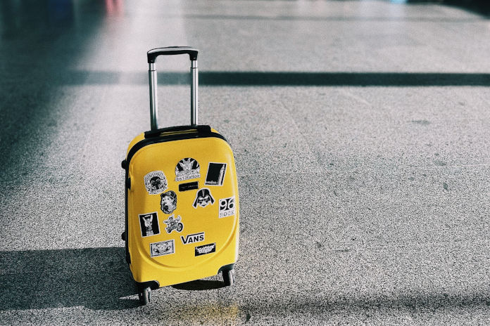 Ein gelber Koffer mit Aufklebern steht auf einem Hallenfußboden.