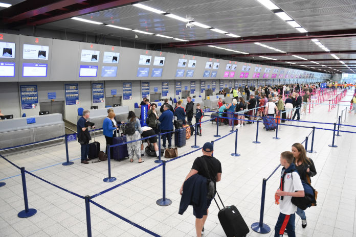 Check-in-Terminals in einer Flughafenhalle. Viele Reisende mit Koffern stehen in Schlangen oder gehen dorthin.