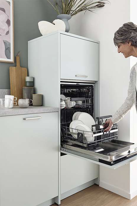 Eine Frau zieht den Korb einer Geschirrspülmaschine aus dem Gerät. Es ist in der Mitte eines Schrankes verbaut-. 