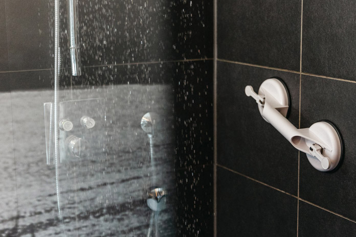Eine schwarz geflieste Dusche, rechts an der Wand ein weißer Haltegriff mit Saugnäpfen.