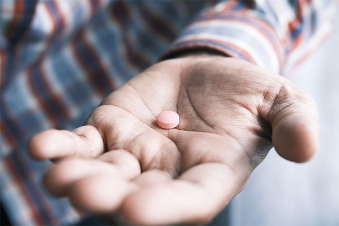 Auf der Innenfläche einer Männerhand liegt eine rosafarbende Pille.