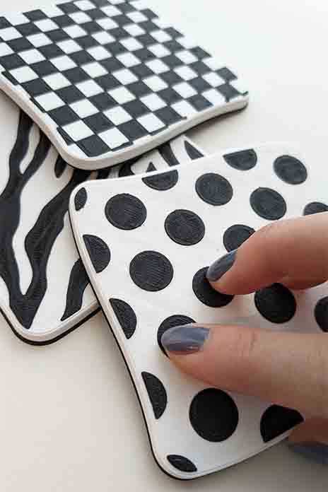 Zwei Finger ertasten auf einer weißen Karte mit schwarzen Punkten das Muster. Im Hintergrund zwei weitere Karten mit Schabrett- und Zebra-Muster.