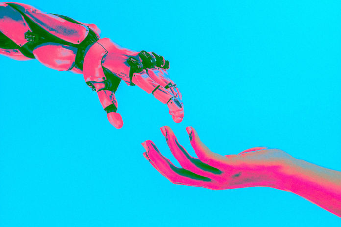 Vor einem hellblauen Hintergrund nähern sich eine menschliche Hand und eine Roboterhand.