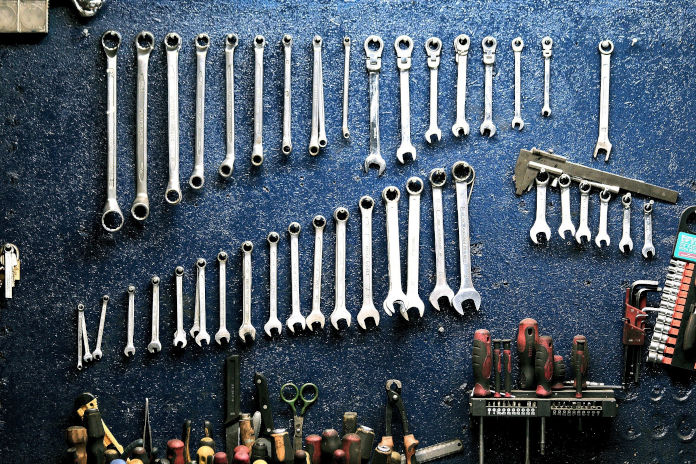 Eine Werkzeugwand mit unterschiedlichen Schraubschlüsseln in verschiedenen Größen an der Wand hängend. Weiter unten im Bild ist weiteres Werkzeug vorhanden.