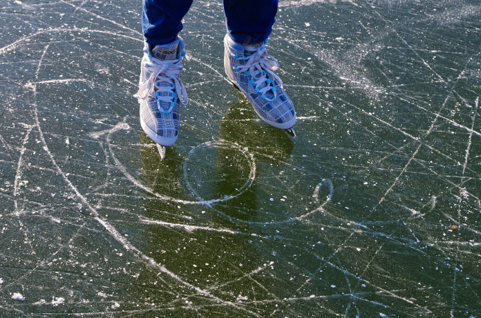 Jemand auf dem Eis, mit Schlittschuhen. Es sind nur die Füße der Person zu sehen.
