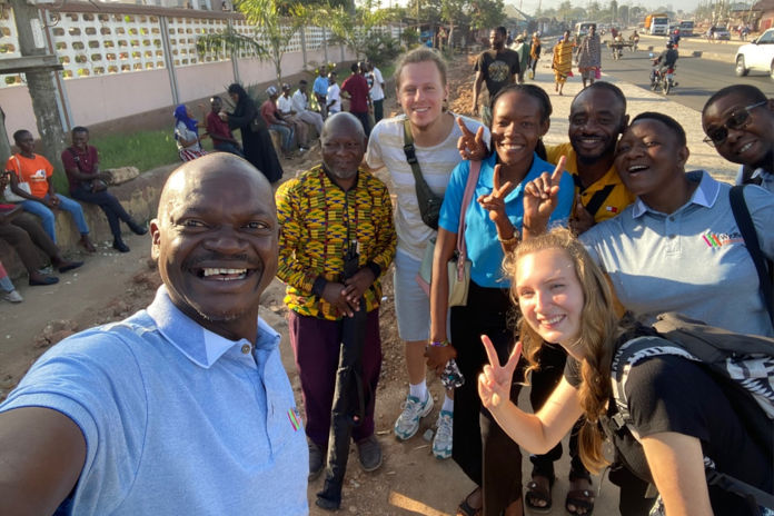 Mehrere dunkelhäutige Personen lächelnd in die Kamera. Darunter zwei junge hellhäutige Personenbei einem Auslandsaufenthalt in Tansania.