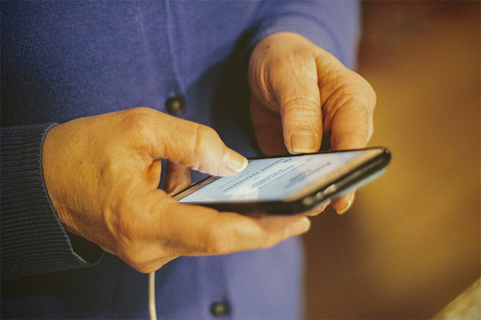 Eine ältere Person hält ein Handy in den Händen.