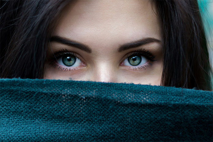 Eine junge Frau mit grün-grauen Augen und dunklen Haaren. Über Mund und Nase trägt sie einen petrolfarbenen Schal.