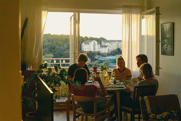 Fünf Menschen sitzen um einen Tisch herum und essen. Hinter ihnen ein großes Fenster mit Blick auf die Stadt.