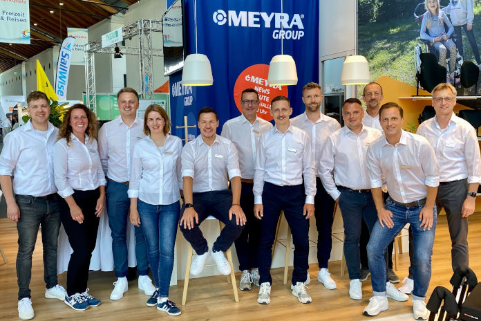 Das Team von Meyra mit 12 Mitgliedern vor einem Messestand von Meyra. Alle lächeln und stehen in einem Halbkreis.